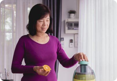 A senior woman stands in a kitchen usings a juicing machine to make fresh orange juice.